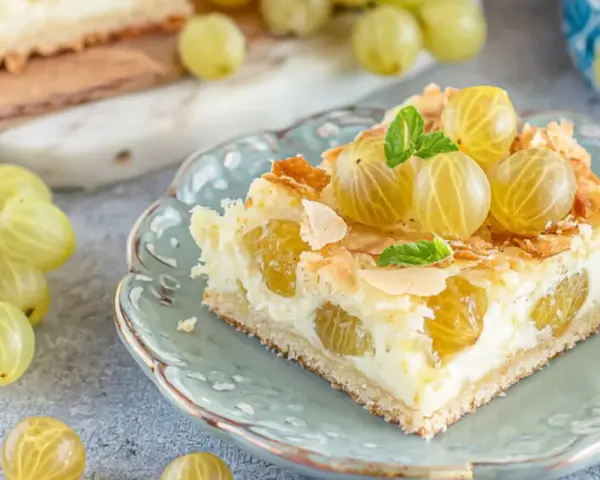 Ein Stück von die besten stachelbeerkuchen, garniert mit frischen Stachelbeeren und Mandelsplittern, auf einem zartblauen Teller.