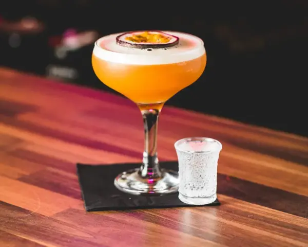 Orzeźwiający passion fruit martini z pianką i plasterkiem owocu, obok kieliszek wody gazowanej. Idealny na letnie wieczory.
