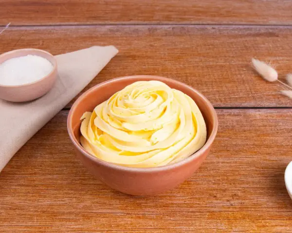 Una ciotola piena di soffice crema al burro, con zucchero in due piccole ciotole e decorazioni di erba secca su un tavolo di legno.
