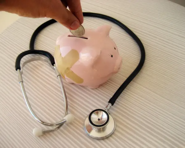 Salvadanaio a forma di maialino con cerotti, uno stetoscopio e una mano che inserisce una moneta. Simboleggia il dottore stipendio e la cura delle finanze.