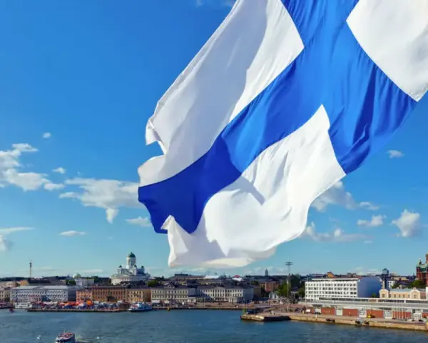 Flaga z niebieskim krzyżem powiewa nad portem w Helsinkach. W tle widać katedrę i inne budynki.