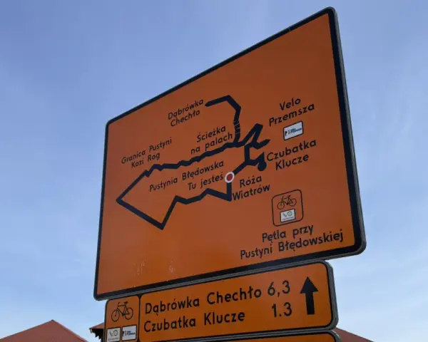 Pomarańczowa tablica z mapą szlaków rowerowych Velo Przemsza. Wskazuje drogę do Pustyni Błędowskiej, Czubatki Klucze i innych miejsc.