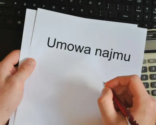 Ręka pisze długopisem na umowie najmu, obok kalkulator i laptop. Czas pomyśleć o podatku od najmu.