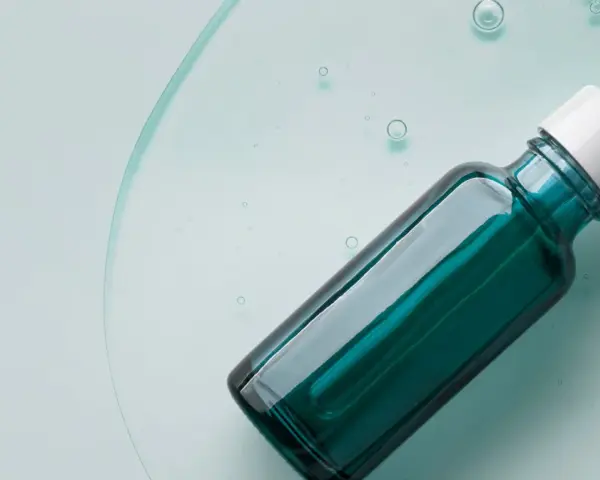 Szklana buteleczka z pipetką, wypełniona zielonym serum, na tle płynu z bąbelkami.
