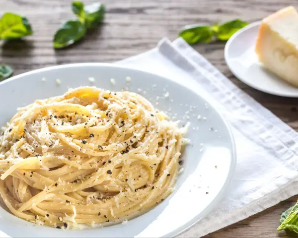 Szybki obiad z makaronem: spaghetti posypane parmezanem i pieprzem, obok kawałek sera i listki bazylii.
