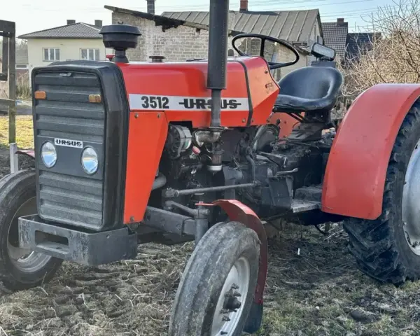 Czerwony ciągnik Ursus 3512 z czarną maskownicą i siedzeniem, stojący na ziemi.