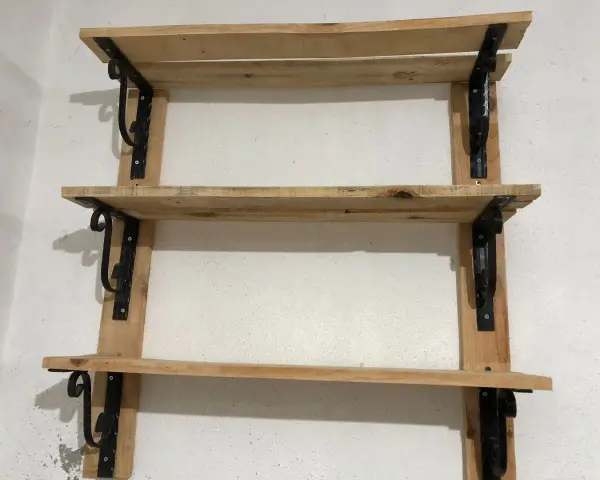 Scaffali fai da te garage: tre ripiani in legno grezzo, fissati a parete con staffe nere decorative. Perfetti per organizzare attrezzi e materiali.