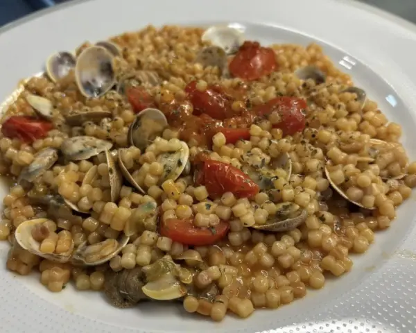 Un piatto invitante di fregola con vongole, pomodorini e prezzemolo, pronto per essere gustato.
