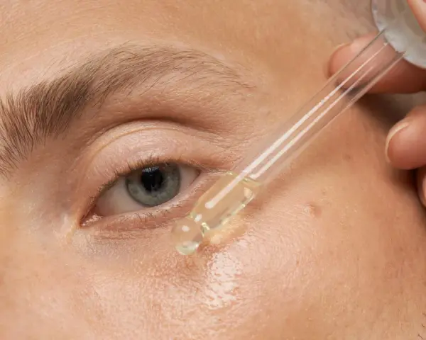 Nahaufnahme eines Auges, auf das ein Tropfen Öl aus einer Pipette aufgetragen wird.