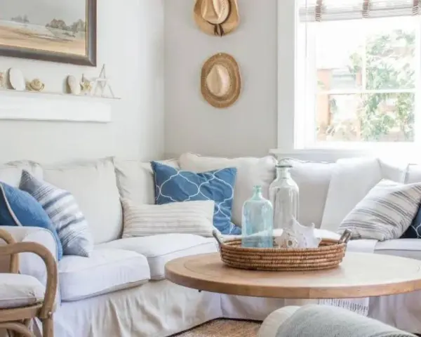 Un accogliente soggiorno con arredamento coastal: divano bianco, cuscini blu e bianchi, tavolino in legno e decorazioni marine.