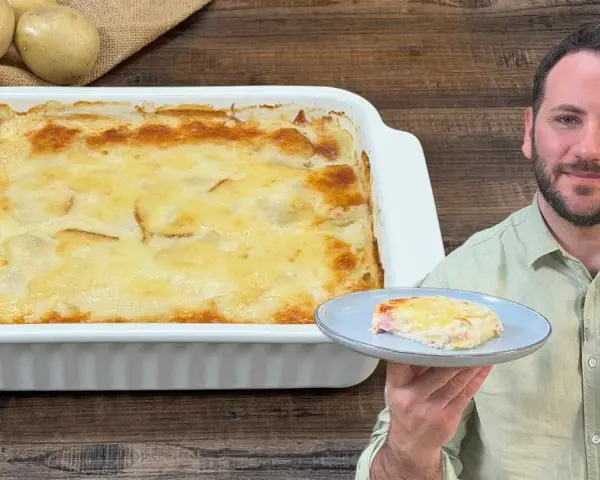 Un uomo sorride mostrando una fetta di parmigiana di patate appena sfornata, dorata e filante.
