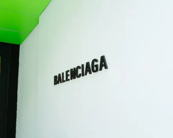 Il logo Balenciaga su una parete bianca, sotto un soffitto verde brillante. Chi è Balenciaga? Un nome che evoca alta moda e design audace.