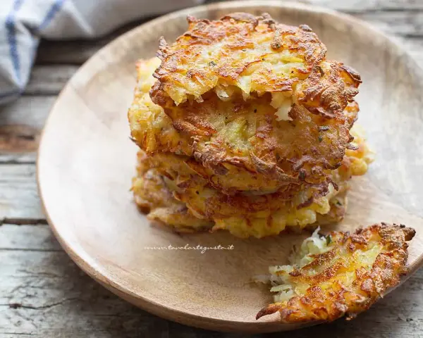 Una pila di dorate frittelle di patate, croccanti fuori e morbide dentro, servite su un piatto di legno.