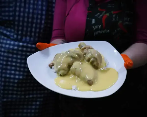 Porcja potrawki z kurczaka w kremowym sosie, podana na ryżu. Danie prezentowane na białym talerzu, trzymanym przez osobę w pomarańczowych rękawiczkach.