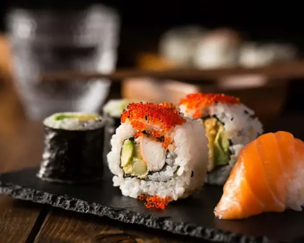 Pyszne rolki sushi z łososiem i ikrą, a obok tradycyjne dodatki do sushi.