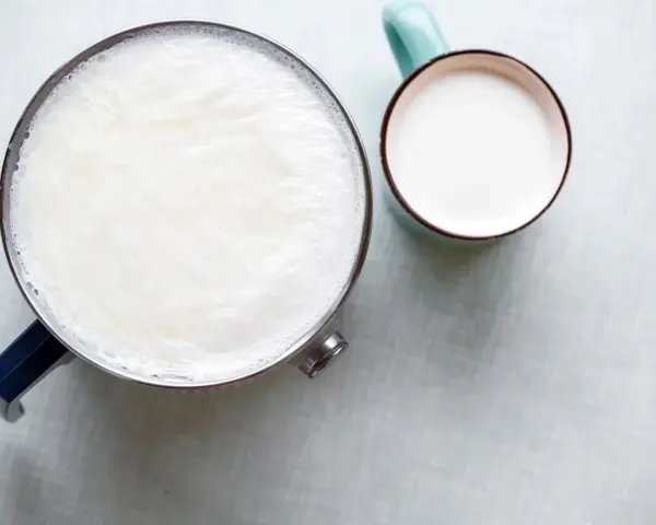 Un pot de lait chaud avec une fine peau de lait à la surface, à côté d'une tasse remplie de lait frais.