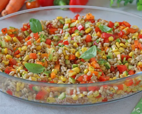 Insalata di farro colorata con mais, peperoni, zucchine e carote, guarnita con foglie di basilico fresco. Un piatto estivo e salutare.