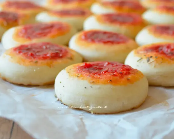 Pizzette fatte in casa, piccole e invitanti, con un soffice impasto e un tocco di pomodoro e erbe aromatiche.