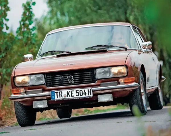 Klasyczny brązowy Peugeot 504 Coupe jedzie po krętej drodze wśród zieleni.