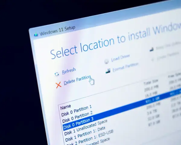 Instalator Windows 11 pokazuje opcje zarządzania partycjami. Kursor myszy wskazuje opcję "Usuń partycję", przygotowując do formatowania dysku.