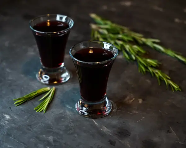 Dwa kieliszki ciemnego, aromatycznego nalewki z czernic, ozdobione gałązkami rozmarynu.