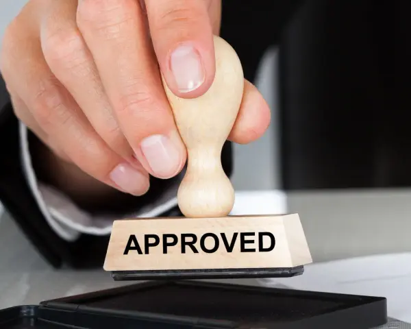 Dłoń z pieczątką "APPROVED" nad poduszką z tuszem. To symbol zatwierdzenia, jak certyfikat AEO.