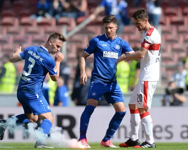 Piłkarze Karlsruher SC w niebieskich strojach, jeden z nich z numerem 3, otoczeni dymem z rac.