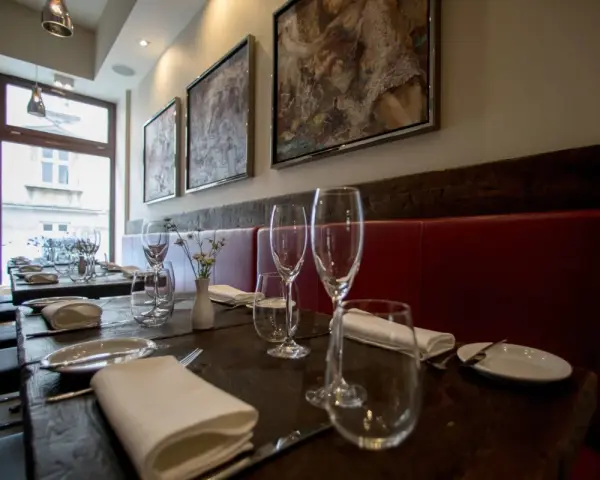 Elegancko nakryte stoły w restauracji z gwiazdką Michelin w Polsce. Czerwone obicia, obrazy na ścianach i kieliszki zapraszają na wyjątkowe doznania kulinarne.