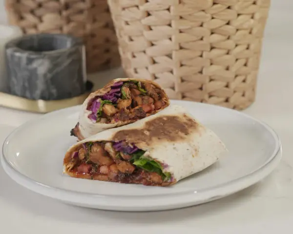 Kebab zawinięty w tortillę, przekrojony na pół, z widocznym nadzieniem z mięsa, warzyw i sosu.