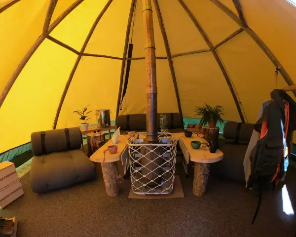 Mysig interiör i ett tipi-tält på Sorsele camping. Här finns sittplatser, ett bord och en kamin för värme.