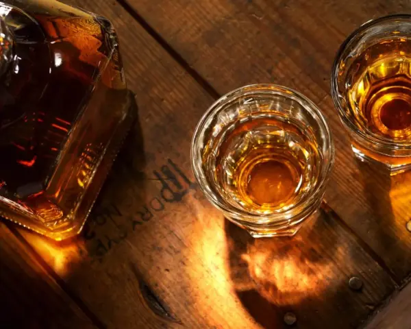 Butelka i dwa kieliszki z bursztynowym płynem, przypominającym koniak lub whisky, stoją na drewnianym blacie.
