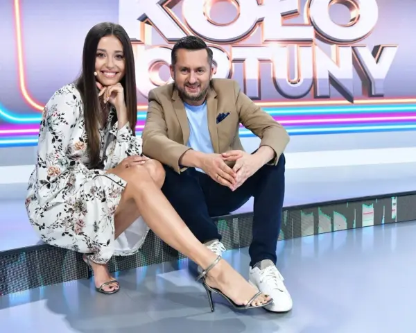 Uśmiechnięta para na planie "Koło Fortuny kto ubiera". Ona w kwiecistej sukience i sandałkach, on w marynarce i jeansach.