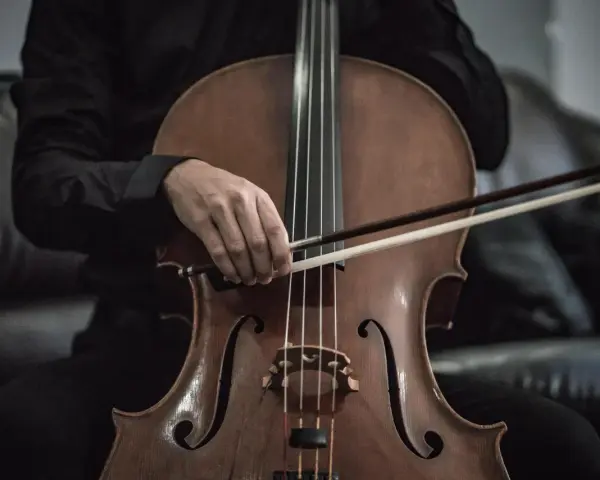 Eine Hand hält den Bogen über dem Violoncello-Instrument, bereit, die Saiten zum Klingen zu bringen.