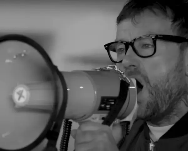 Un homme avec des lunettes et un mégaphone, sa voix résonne. Le groupe est en plein concert.