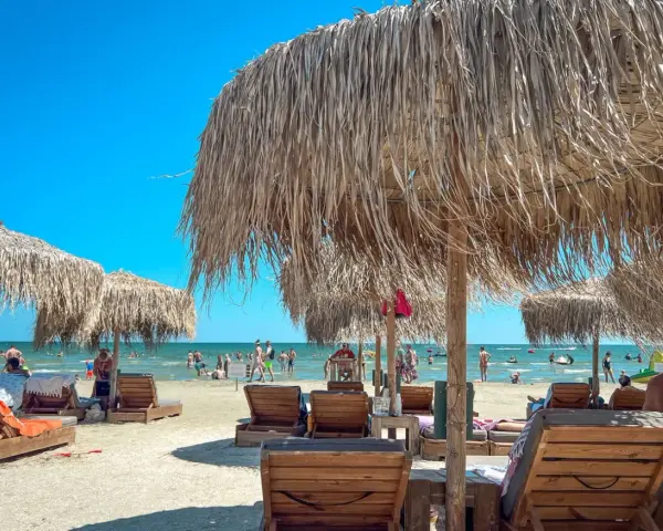 Słoneczny dzień na plaży w Rumunii nad Morzem Czarnym. Leżaki i parasole z trawy zapraszają do odpoczynku.