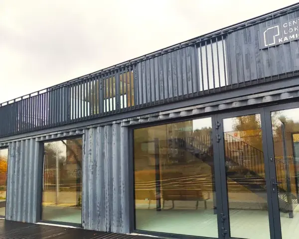 Nowoczesne centrum lokalne Kamionek, zbudowane z kontenerów. Ten innowacyjny kamionkowy materiał budowlany tworzy przestrzeń z przeszklonymi fasadami i balkonem.