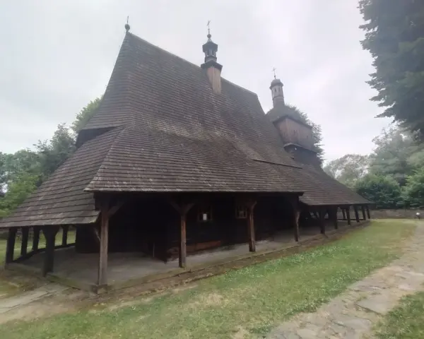 Drewniany kościół w Sękowej z charakterystycznym, wielospadowym dachem krytym gontem, otoczony zielenią.