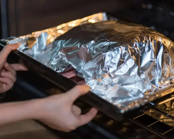 Mains dans un plat recouvert d'aluminium au four, prêt à cuire.