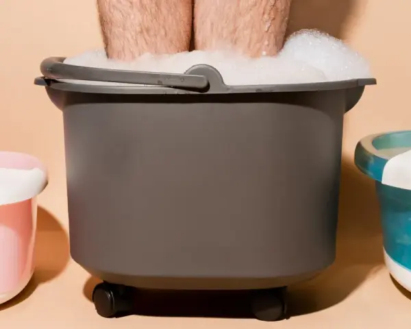 A person's legs are submerged in a foamy foot bath, part of a home foot detox setup with other foot spa machines.