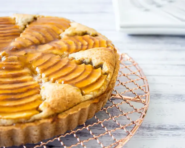 Deliciosa tarta de pera francesa, con peras laminadas y glaseado dorado, enfriándose sobre una rejilla de cobre.