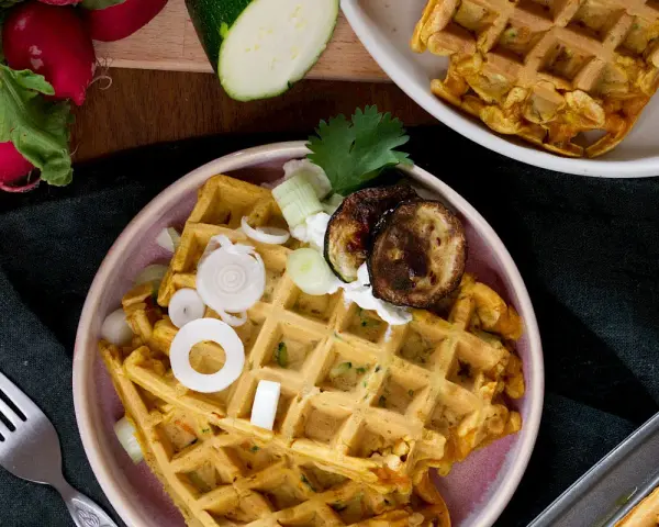 Herzhafte Waffeln mit Zucchini, Zwiebeln und gegrillten Auberginen, garniert mit Kräutern und einem Klecks Joghurt.