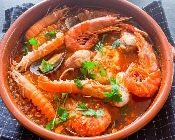 Deliciosa zarzuela de pescado con gambas, mejillones y cigalas en una cazuela de barro, adornada con perejil fresco.