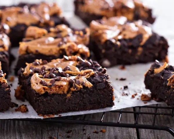 Pyszne brownie z bananami i masłem orzechowym, posypane czekoladowymi kropelkami, kuszą na czarnej kratce.