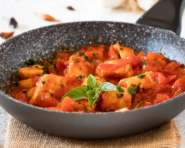 Bocconcini di pollo in padella con pomodoro e basilico, un piatto succulento pronto per essere gustato.