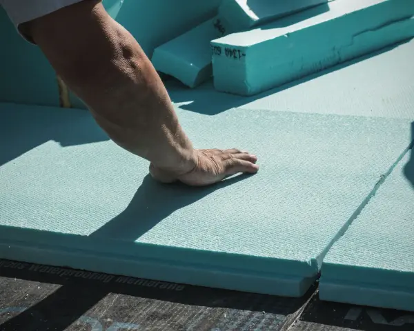 Mano che posiziona pannelli isolanti azzurri, materiali per cappotto termico, su membrana impermeabile.