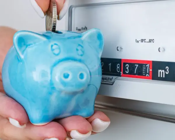 Ahorra con el plan renove calderas gas natural. Una mano deposita una moneda en una hucha cerdito azul junto a un contador de gas.