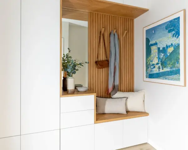 Ideas para decorar recibidor pequeño: banco de madera, espejo, perchero con bolso y bufanda, cuadro y armarios blancos.