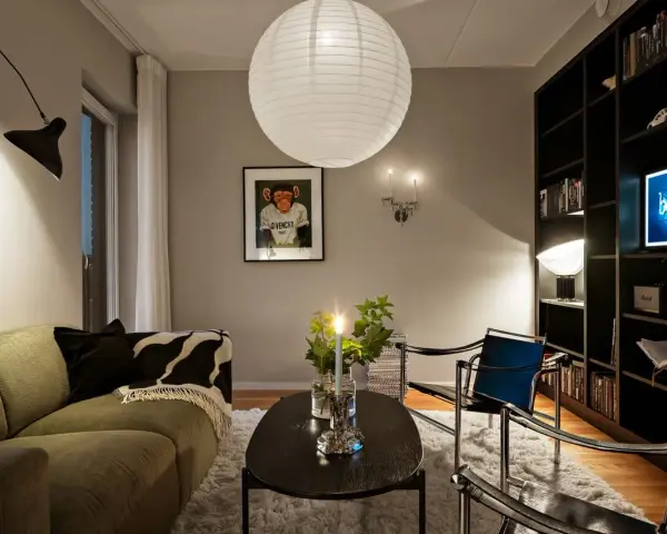 Mysig vardagsrumsmiljö med en stor taklampa, en svart vägglampa och en bokhylla full med böcker. Perfekt lampor inspiration för ditt hem.