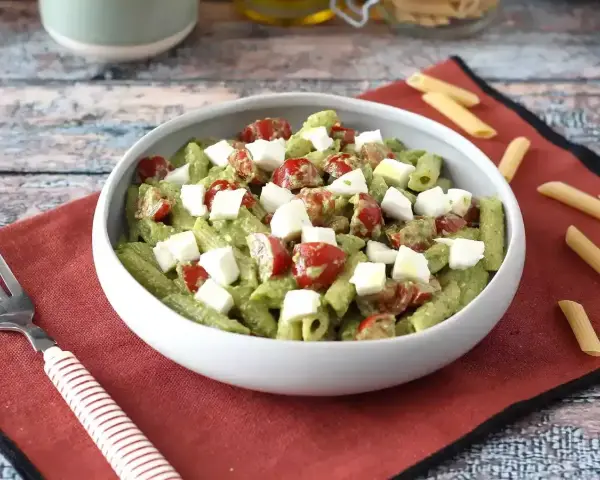 Makaron z pesto ze słoika przepis: penne z zielonym pesto, pomidorkami koktajlowymi i kostkami mozzarelli w białej misce.