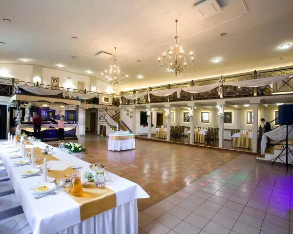 Elegancka sala weselna z długim stołem, ozdobionym złotą podkową. W tle bar i schody prowadzące na antresolę.
